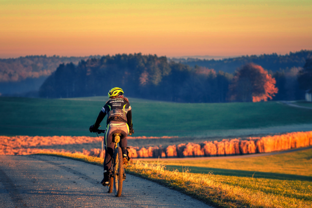 Ciclista na estrada, desfrutando de um passeio de bicicleta em meio a áreas verdes exuberantes, praticando ciclismo de estrada ao ar livre.