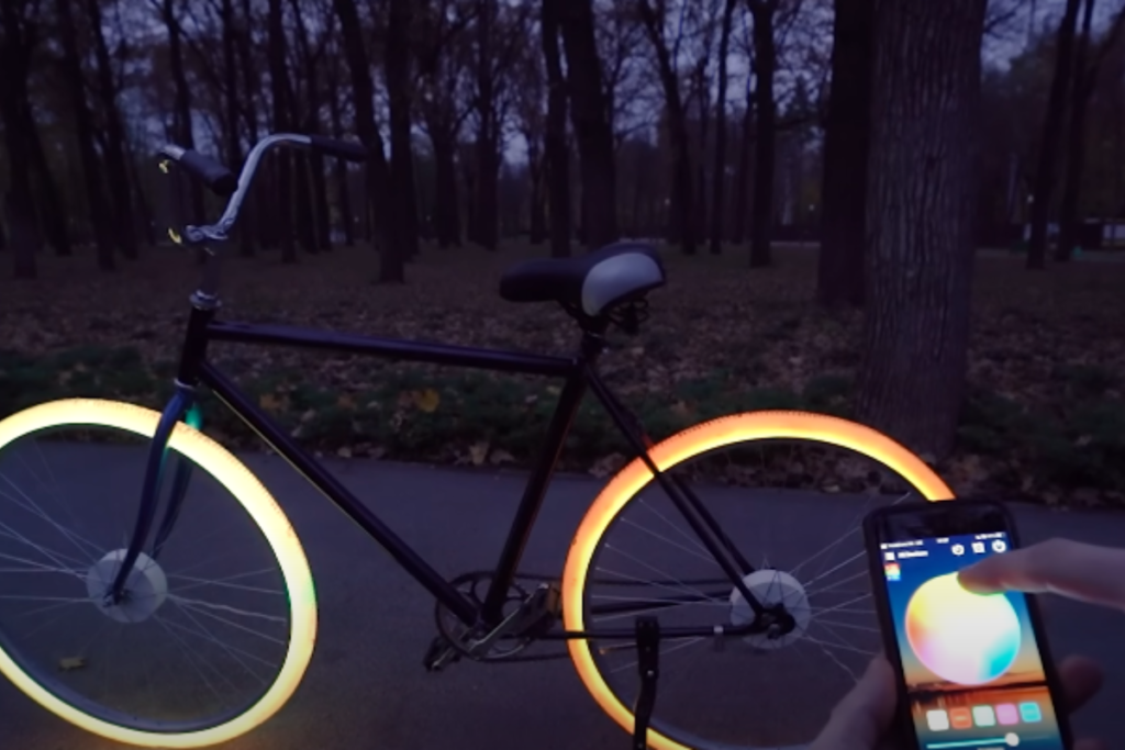 A bicicleta em si é elegante e moderna, com um quadro aerodinâmico e detalhes cromados. Seu design minimalista é acentuado pelas luzes brilhantes que emanam das rodas. As cores contrastantes entre as rodas adicionam um toque de estilo e personalidade à bicicleta.